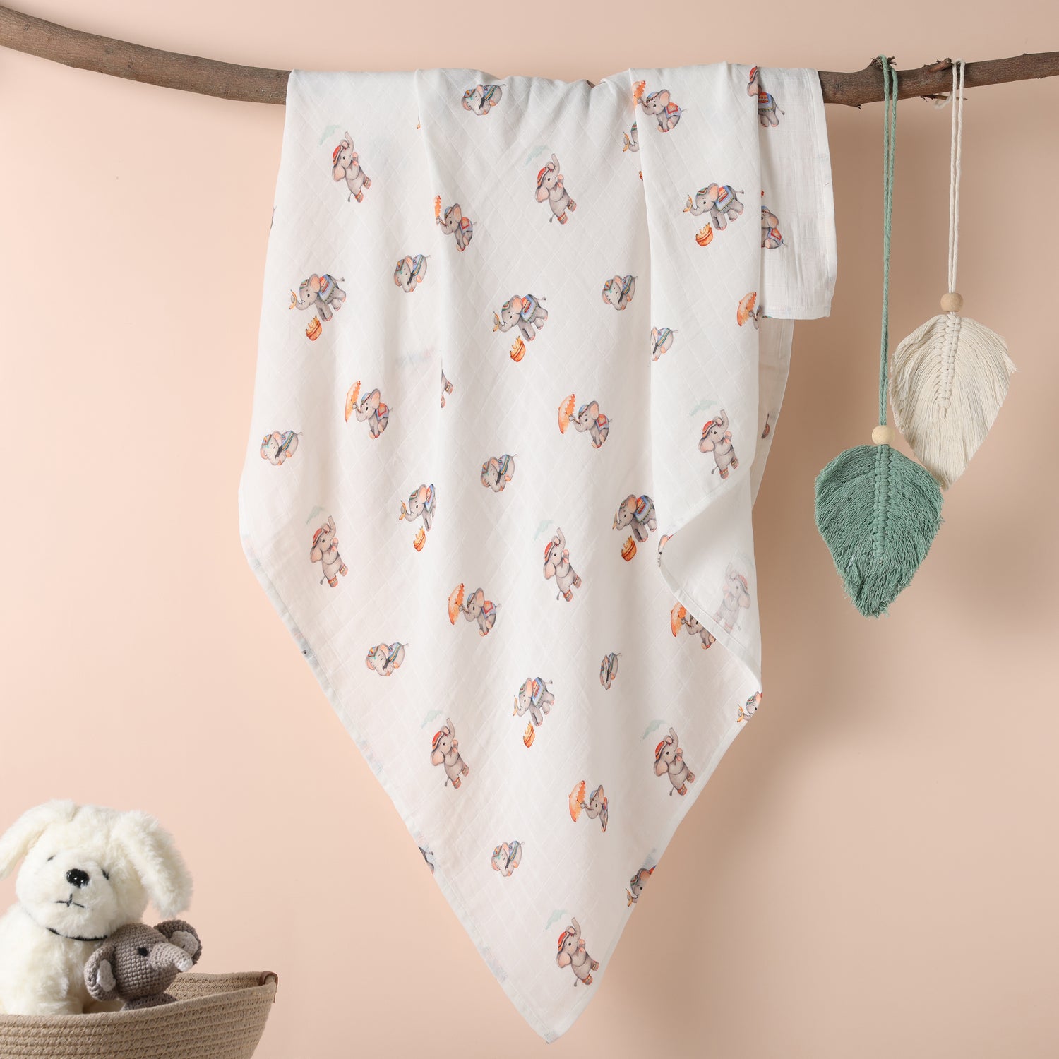 Baby blanket with animal pattern hanging on a branch, next to a teddy bear and leaf decorations.